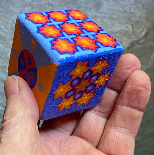 Part of a hand holding a painted cube. 