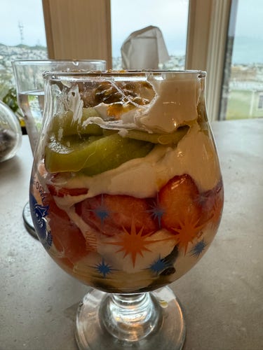 A layered parfait in a tulip glass. Visible are blueberries, strawberries, kiwis, and grapefruit slices. 