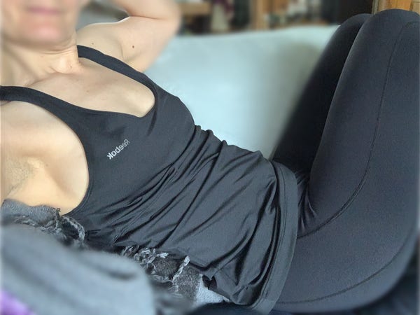 Reclining on sofa, knees up and feet on furniture. Holding camera out to the side. Other arm stretch behind my head. Wearing black Lycra leggings and a Lycra top that is bra shaped up top and looser around the middle. Side boob visible. 