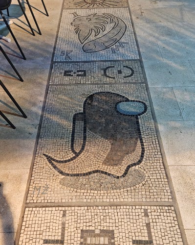 A mosaic on a sidewalk depicting an Among Us ghost crew member.
The mosaic is part of a long strip along the harbour with various motives