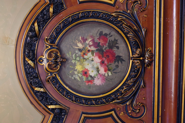 View of the painted ceiling of one of the older buildings at Utrecht University, the Drift 23. Painting is of flowers, painting is surrounded by intricate woodwork painted in golden-brown and black.