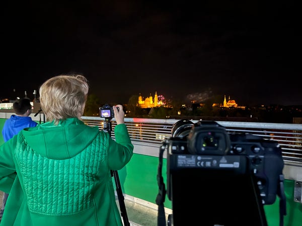 Menschen machen mit Kameras auf Stativen Bilder von einem Feuerwerk am Horizont