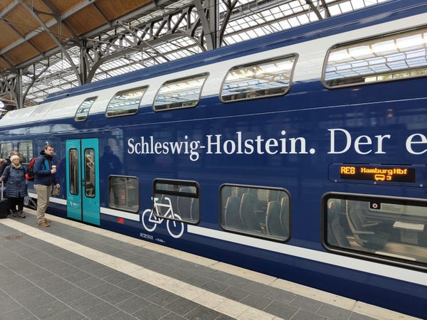 Doppelstock-Regionalzugwagen am Bahnsteig in Lübeck. Dunkelblaue Grundfarbe mit türkisen und weißen Akzenten.