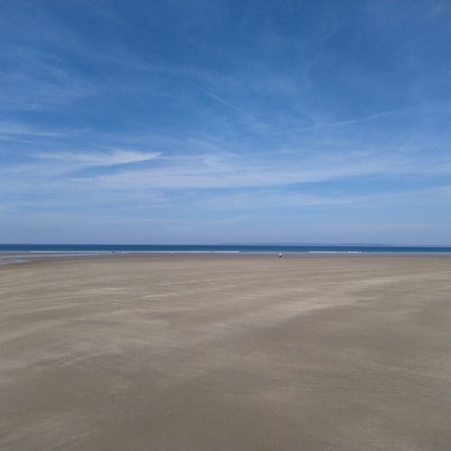 Une plage de sable clair, au loin on voit la mer.