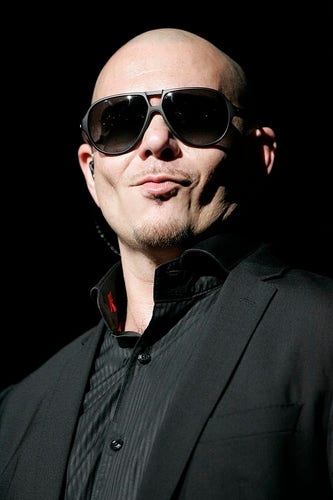 If sex crime had a face, this would be it. Pitbull is a man with a smooth head and carefully styled thin tufts of hair on his face. The whole ensemble just makes his head look like an actual penis. Here we see the penis wearing glasses that are annoying but it's difficult to articulate why. He's wearing what looks like a black shirt and a black vampire cape - presumably so he stalk women in the night. Here we see him doing a smile that suggests he's just seen a drunk woman become separated from her friends. 