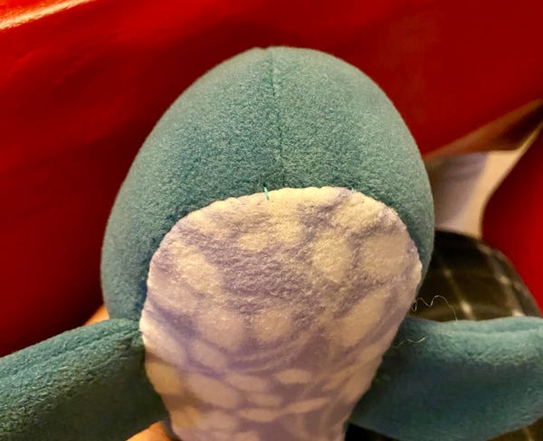 A close-up of a plush toy with green fabric and a patterned underside, against a red background.