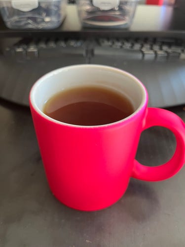 Eine sehr, sehr pinke Tasse. Die Tasse ist mit Tee gefüllt und steht auf einem Schreibtisch.