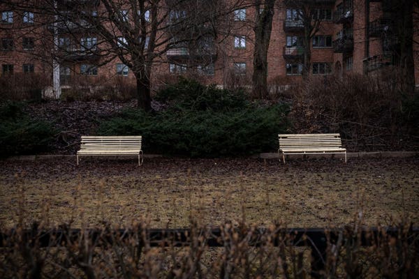 Two empty benches in the rain wet front yard of an apartment building.