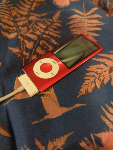 An old, pink ipod lying on a bed.