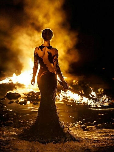 Woman, sword in hand, looking at a lake in fire.

View from behind, she's wearing a very long figure-hugging dress with irregular cutouts.
