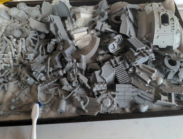 Pile of cleaned resin components for a Acastus Knight Porphyrion from Games Workshop. A toothbrush sits in the lower left of the frame, barely the size of one of the small to medium sized components from the pile. 