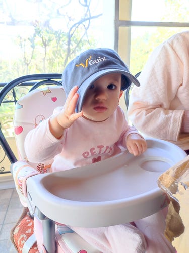 A baby wearing a hat which bears the Guix logo