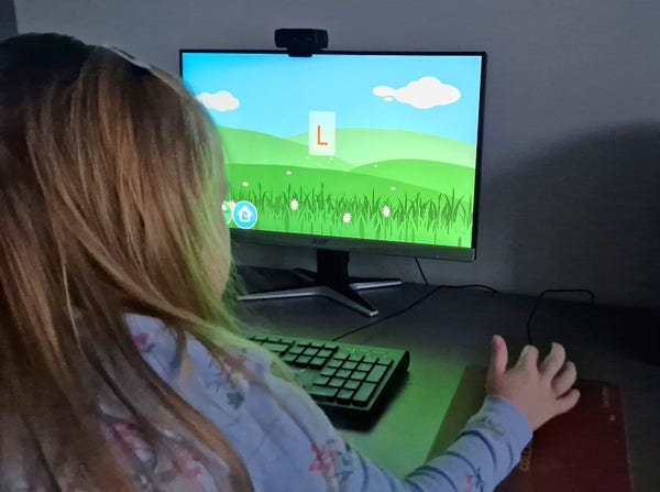 A kid in front of a computer screen holding the mouse. There is a Gcompris module to learn letter on the screen.