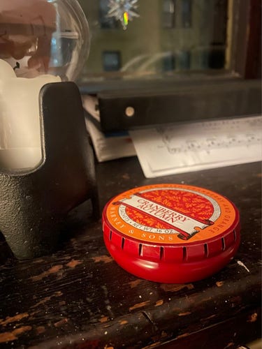 Circular red metal container with lid that has numerous notches cut out of the sides. Lid clamps down to hold the container closed. It releases when someone or something pushes down in the middle.