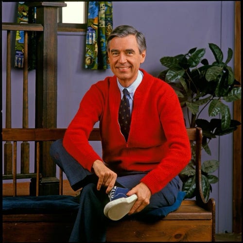 Mister Rogers in a red cardigan removing his shoes.