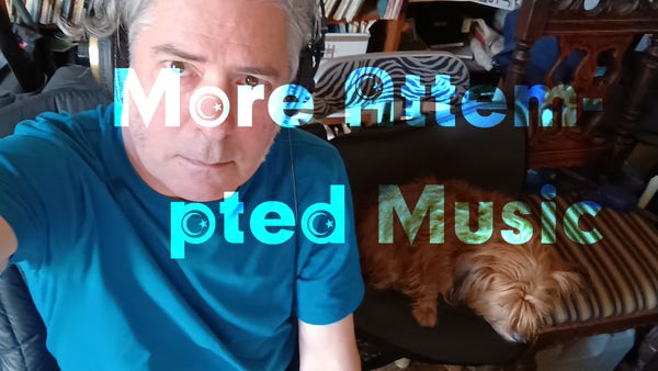 Guy with grey hair and headphones wearing a teal blue t-shirt sits in a dim room, looking serious, next to a small blonde terrier named Coco, who occupies the chair next to him.
The words "More Attem-pted Music" stretch across the image.