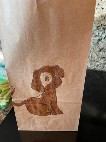 A brown paper lunch bag with a drawing of a brown spotted dog on it