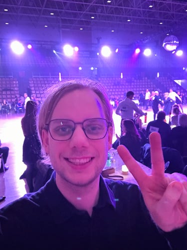 Selfie of me doing the peace sign while people are dancing in the background.