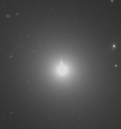A monochrome image of the center area of galaxy M87 with a relativistic jet of material visibly radiating upwards.