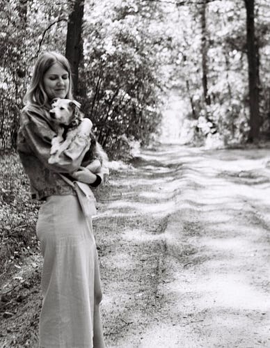 Photo of a woman holding a dog in her arms, forest path in the background.