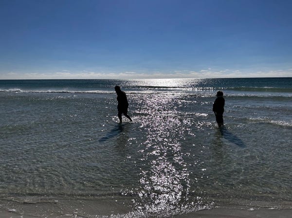 Calm shallow oceanscape, blue sky, silhouettes of two people wading in the water