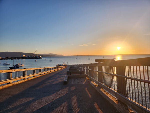 A photo of Taylor Dock and the South Bay Trail over Bellingham Bay heading toward sunset with mostly clear skies.
