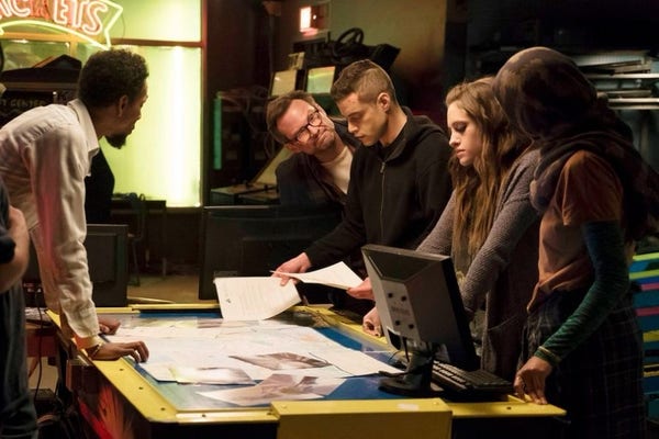 A screenshot of Mr Robot, showing the members of f-society clustered around a computer.