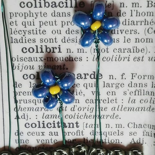 Photo of perlage forget-me-nots on an old dictionary page, part of a tin installation. The flowers are made with the tiniest glass rocailles in lustred blue and yellow.