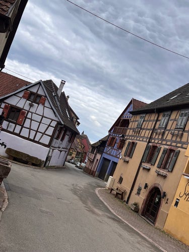 Rue d'un vieux village alsacien avec des maisons traditionnelles à colombages sous un ciel couvert.