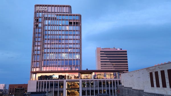 A 15 story glass tower reflecting a setting sun. A smaller tower in background.