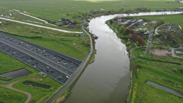 De rivier de Vecht, geflankeerd door een dorpje en polder, kruist over de twaalfbaans A1 via een aquaduct (de Vecht) en ondiepe tunnel (de A1). Het ziet er een beetje onwerkelijk uit.
