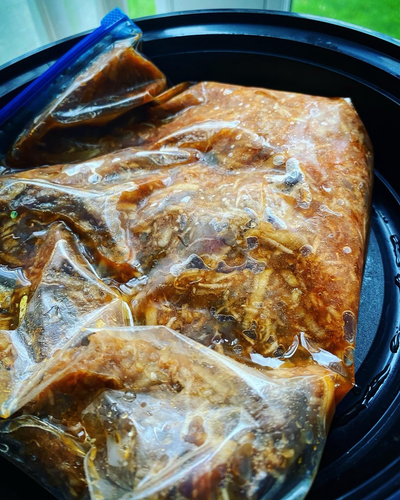 Skirt steak in a bulgogi marinade in a zip top bag in a black round plastic to go container in case it leaked in the fridge the shredded apple and garlic are visible 