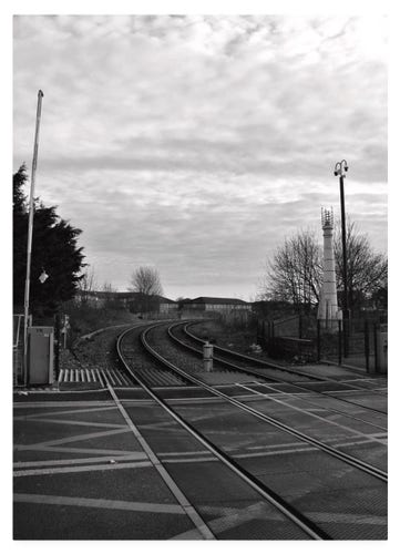 Black and white photograph showing railway tracks at a crossing.  The tracks lead away and around the bend to the right.