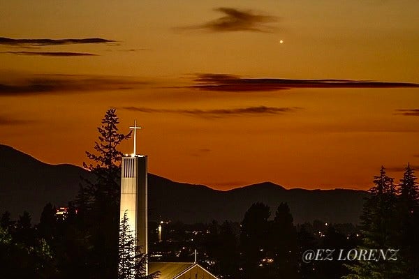 Venus is shining bright in the after sunset orange glow just right to the cross of a Bellevue Church. 
