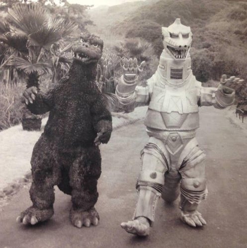 Vintage black and white photo of Godzilla and Mechagodzilla walking down the road together. 