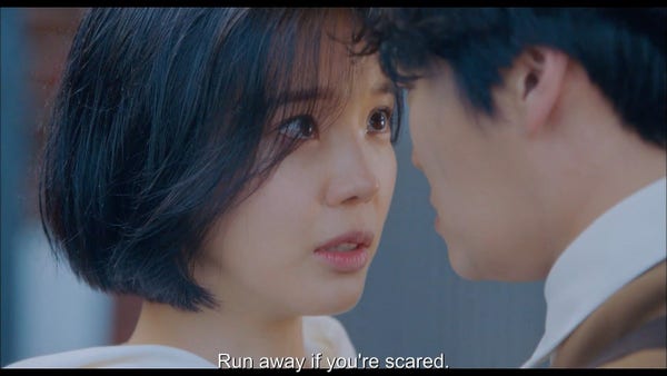 Screenshot of a kdrama showing a couple with subtitle "Run away if you are scared"