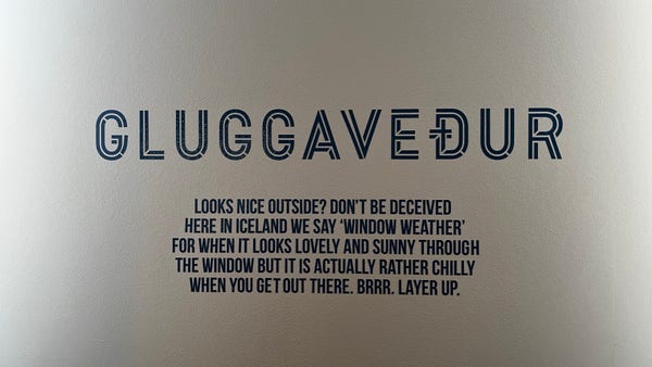 The image contains text on a wall, explaining the Icelandic term "GLUGGAVEÐUR," which means 'window weather'—referring to weather that looks sunny and pleasant from indoors but is actually cold outside. The text advises to layer up.