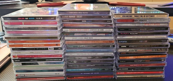 3 stacks of CD cases of at least 16 cases in each stack. Featuring artists like Lenny Kravitz, Kenny G, Lisa Loeb, Vanessa Williams, Dia Frampton, UB40, and more.