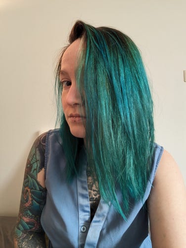 pyrrh with bold, medium aqua hair, in a forget me not blue button front sleeveless blouse. its face is halfway hidden by its hair and the angle of the photo 