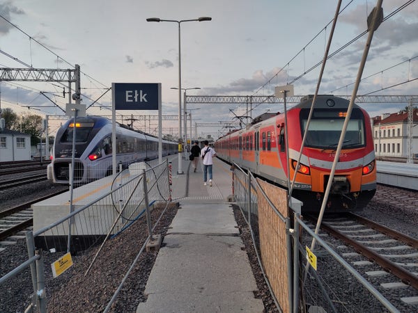 Peron na stacji w Ełku, widok z tymczasowego przejścia między peronami. Po prawej PESA Dart, po lewej EN57 w pomarańczowym malowaniu 