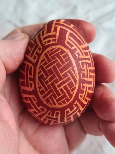 Jajko barwione w cebulaku z wydrapanym wzorem w kształcie przeplatanych linii, ułożonych w kratkę.