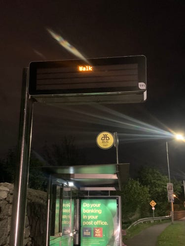 Digital sign over a darkened bus stop that says only WALK 