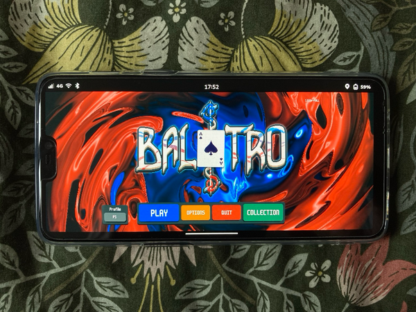 A OnePlus 6 smartphone laying on a flower linen, showing the Balatro game main menu. The Balatro logo is in foreground with buttons to start the game underneath.