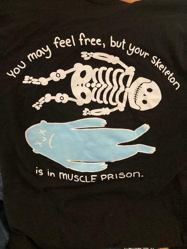 A shirt with a skeleton that says you may feel free but your skeleton is in muscle prison 