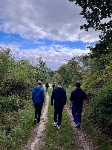 Fünf Menschen laufen durch einen grünen Wald, von hinten, drei im Vordergrund und zwei im Hintergrund.