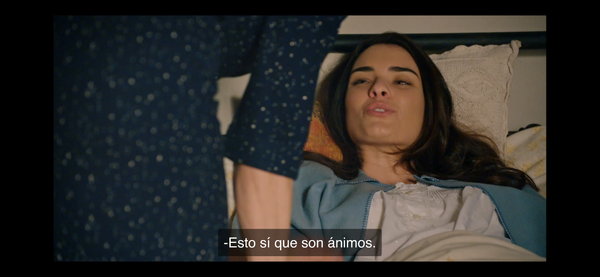 Screenshot of Marta (hardly in shot and from behind) leaning over Fina who is lying in bed, less makeup and hair down, she’s recovering from being stabbed 

The caption reads “esto sí que son ánimos”