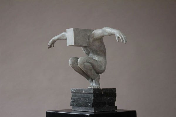 A sculpture of a man squatting with his arms wide open. His head has been replaced with a cube.