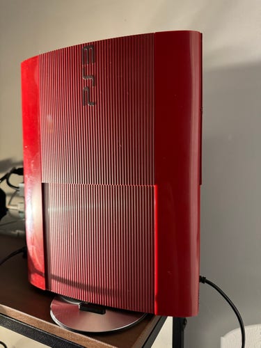 A red super-slim PS3 stood vertically on a shelf.