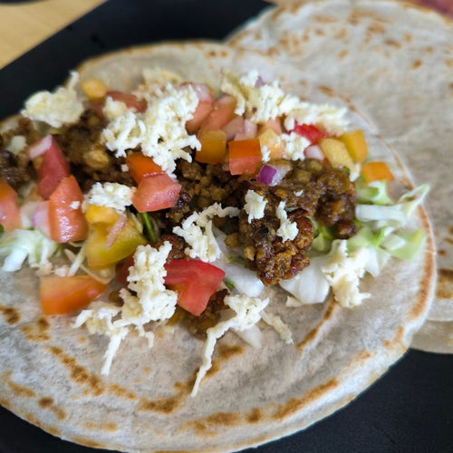 Toasted tortilla with cabbage, tomatoes, onion, tofu that looks like ground beef, and cheese