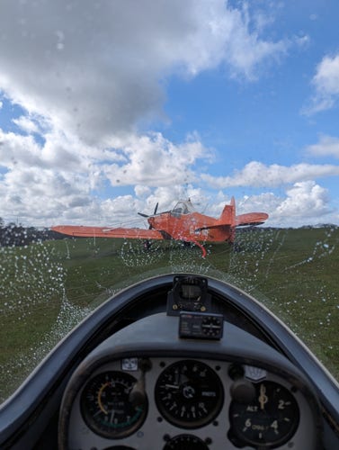 View from inside a glider on the ground, there's rain on the canopy and a bright orange tug aircraft is in front.